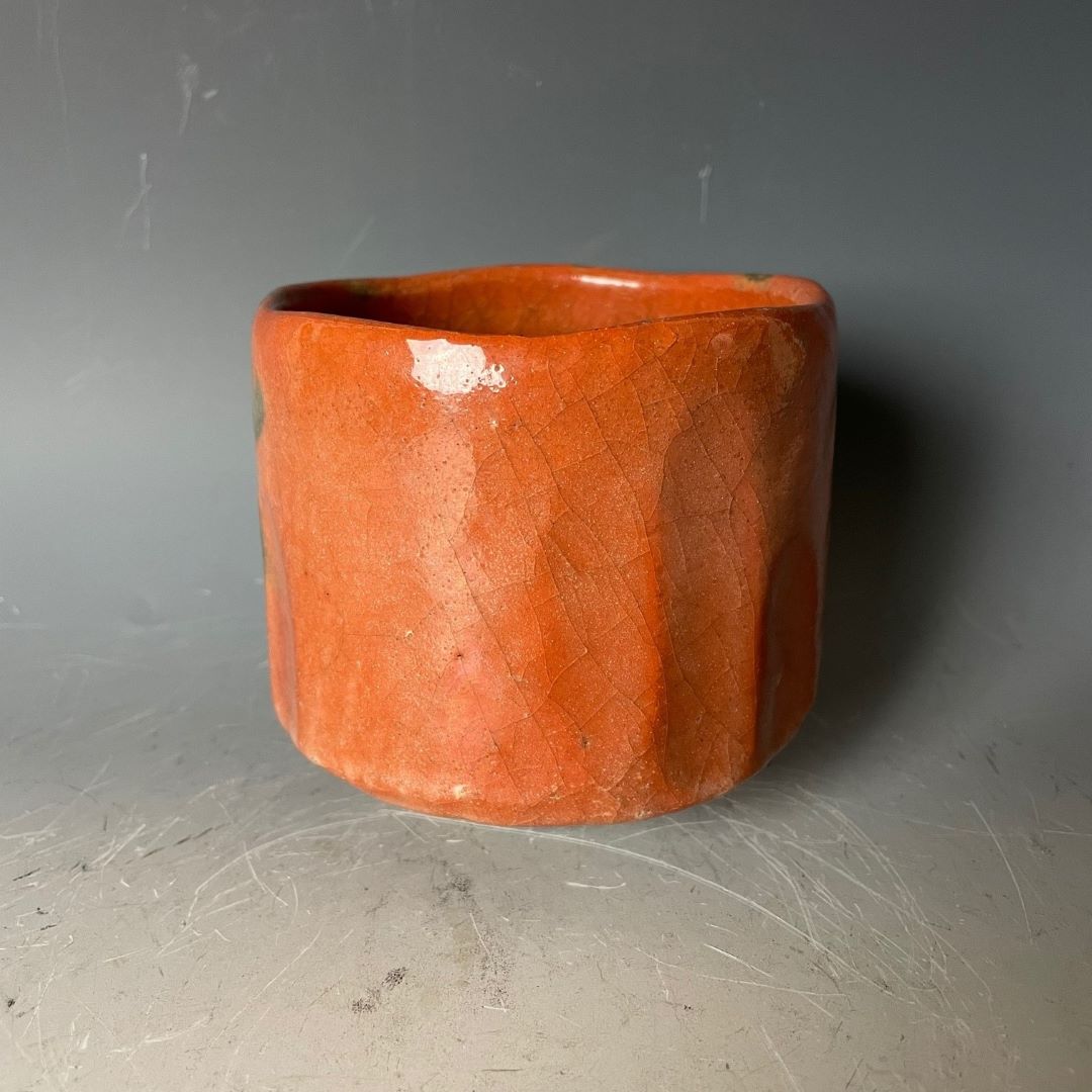 A traditional Japanese Akaraku-style Raku yaki tea bowl used in tea ceremonies, featuring a vibrant orange glaze with abstract black patterns, showcasing the unique pottery craftsmanship.