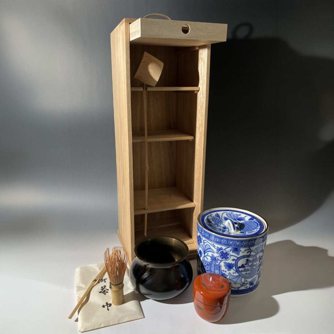 Wooden shelf with tea-making items including a blue and white teapot, black bowl, and red candle on a gray background.