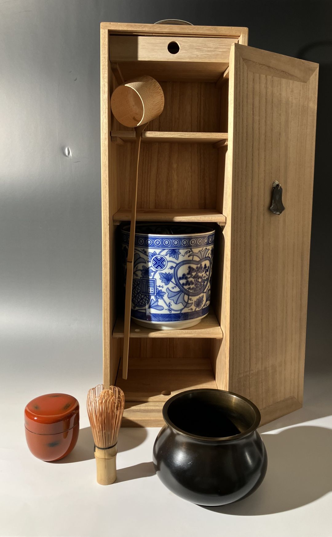 Wooden cabinet with tea-making items including a black pot, red container, and blue and white ceramic jar.