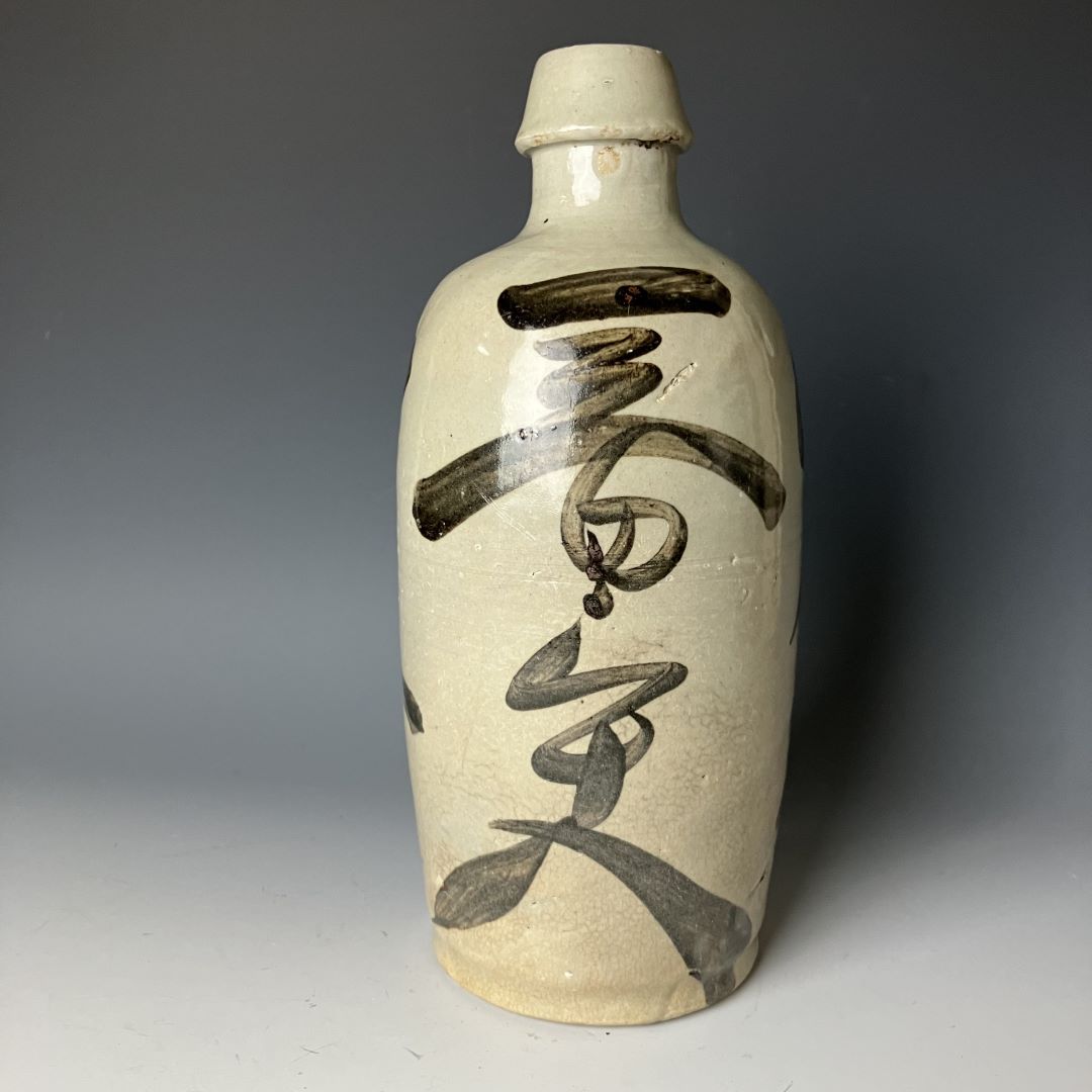   A side view of an antique Japanese Tokkuri sake bottle with kanji calligraphy, featuring a crackled glaze finish.