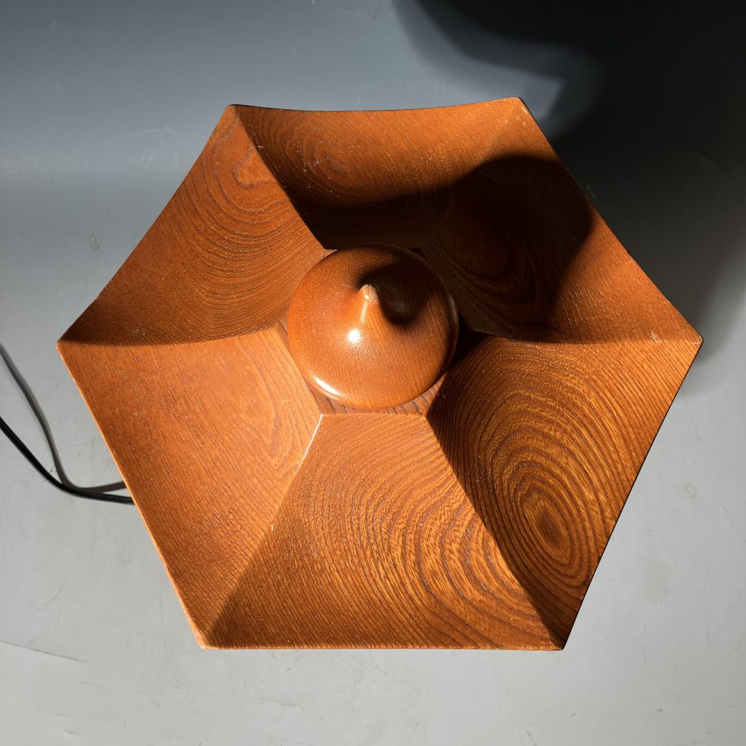 Top view of a vintage Japanese wooden pagoda lantern showing its hexagonal roof design with smooth wood grain patterns and a central finial, highlighting traditional craftsmanship and elegant geometry.