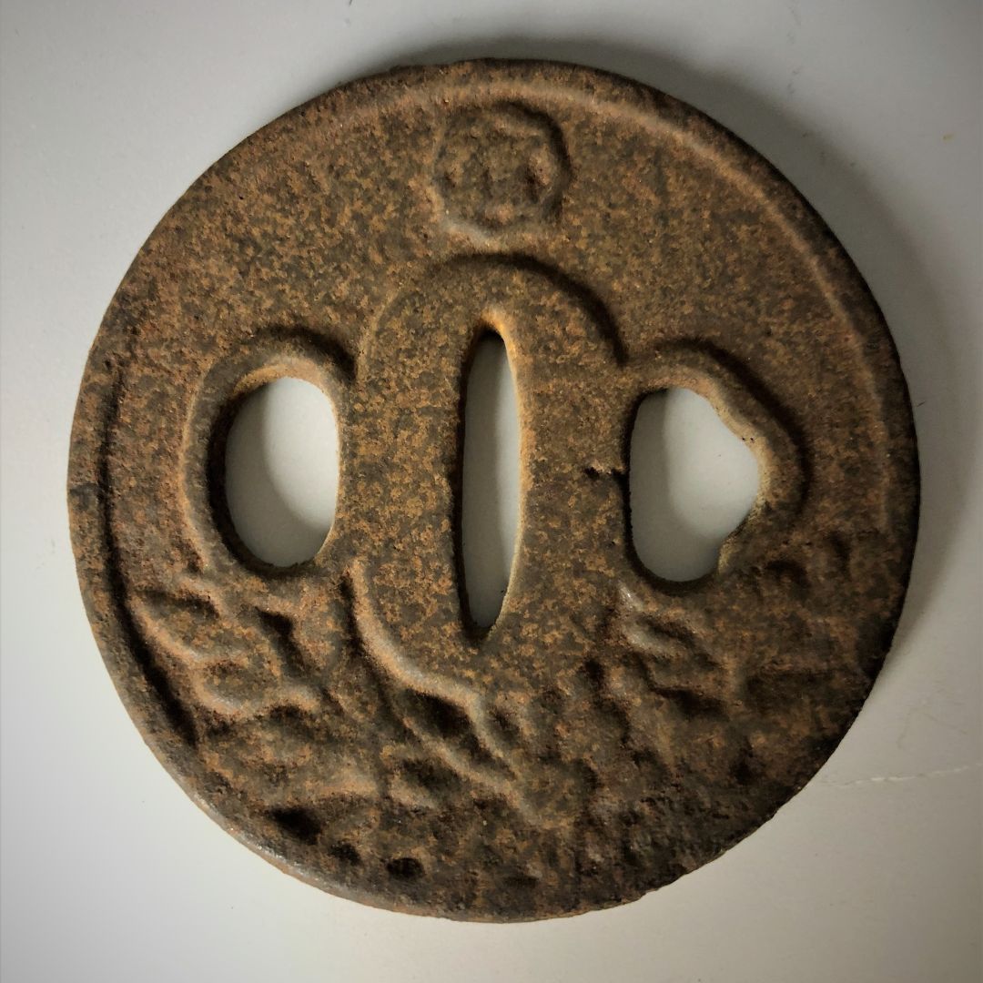 Rust-colored metal tsuba with intricate designs on a white background