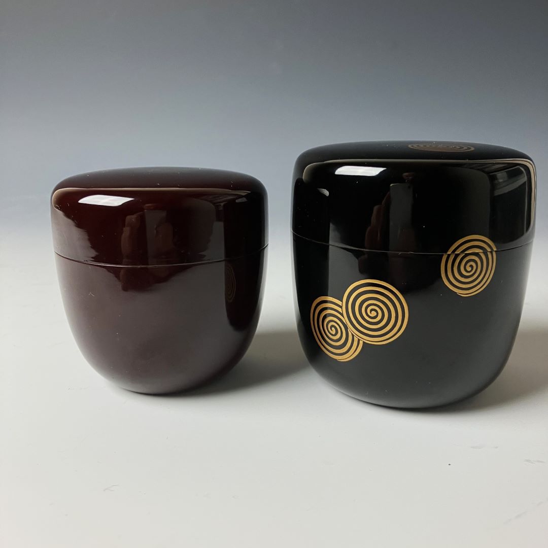 Two 19th-century Japanese lacquered makie natsume tea caddies in black and brown with gold floral designs, showcasing traditional craftsmanship and elegance.