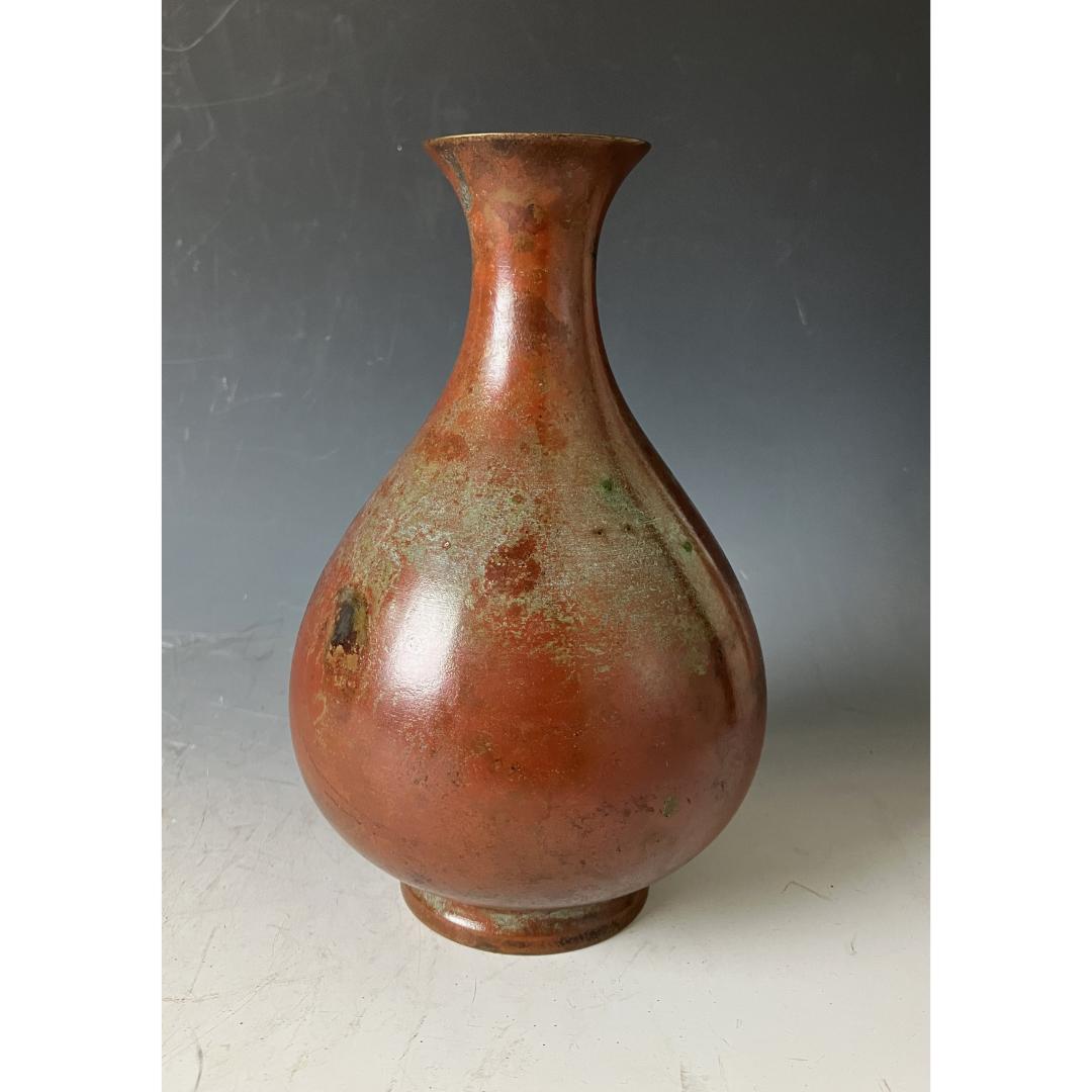 An aged copper vase with green patina accents, displayed against a grey backdrop.