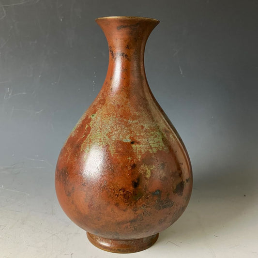 A tarnished copper vase with a patina finish on a grey background.