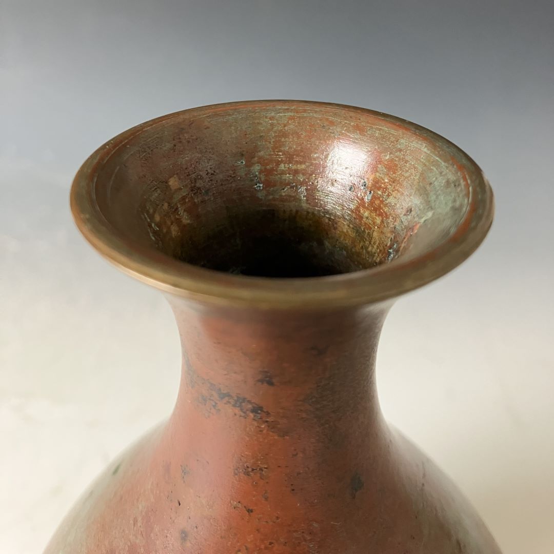 Close-up of the top of a copper vase, highlighting the patina inside the rim against a soft background.