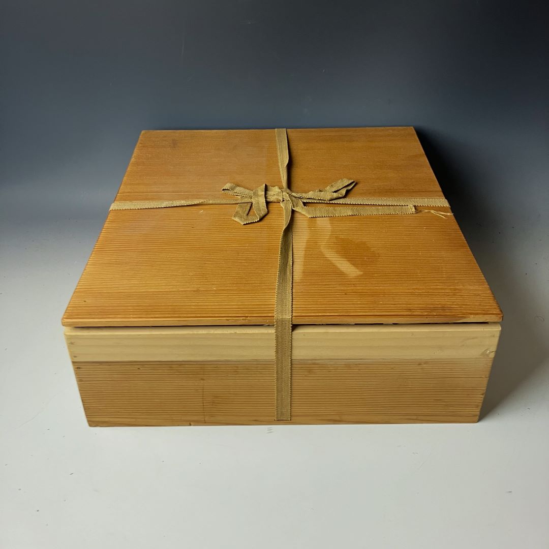 A natural-finish wooden box tied with a beige cloth ribbon, likely used for storing delicate ceremonial items.