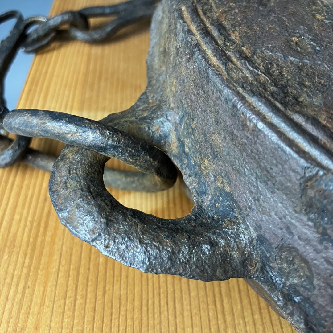 A detailed view of the handle and chain of an antique Waniguchi gong, showing the textured, oxidized metal against a wooden base with a visible grain pattern.
