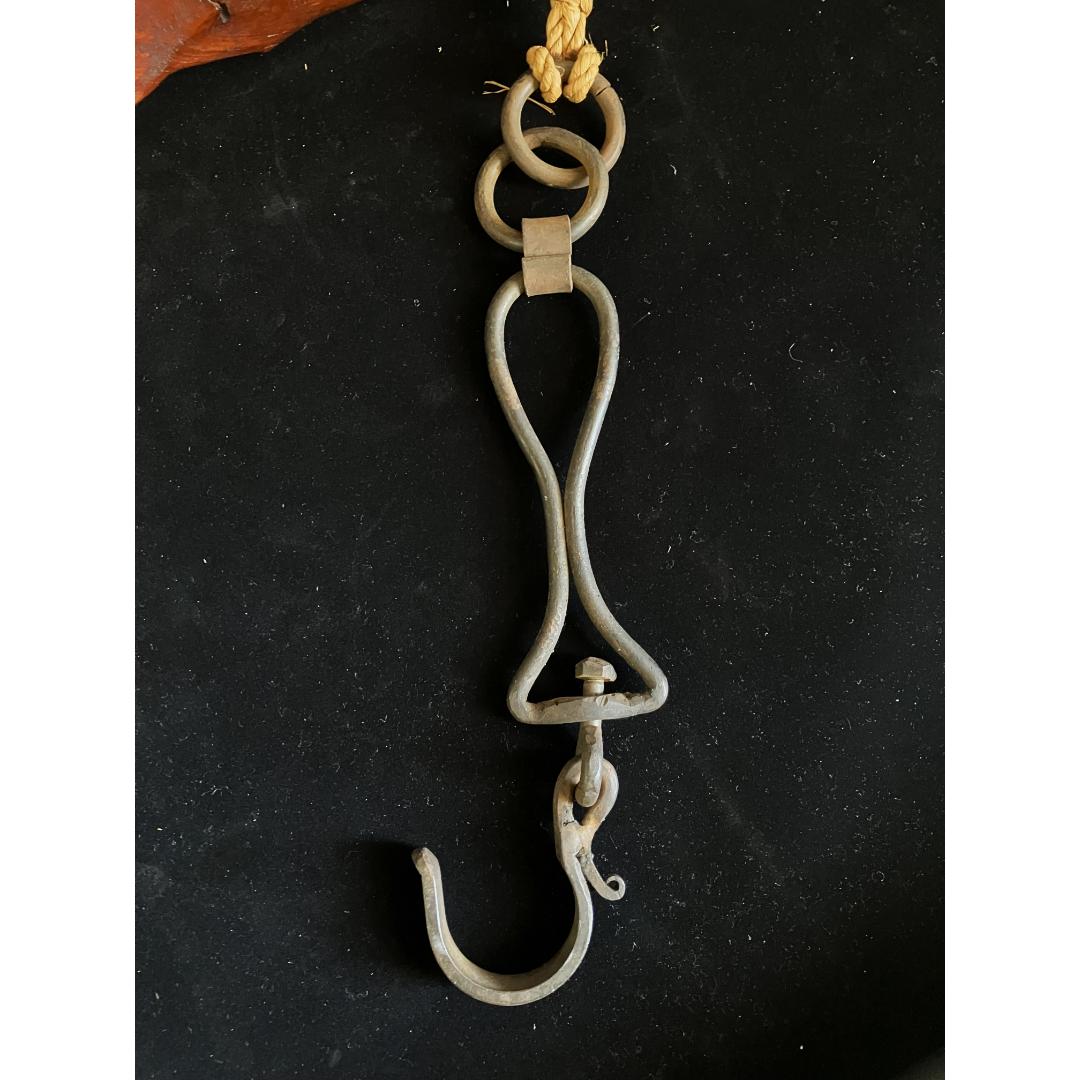 A traditional iron kettle hook (jizaikagi) with a twisted design and a loop on top, attached to a natural fiber rope with a knot, presented on a black background.