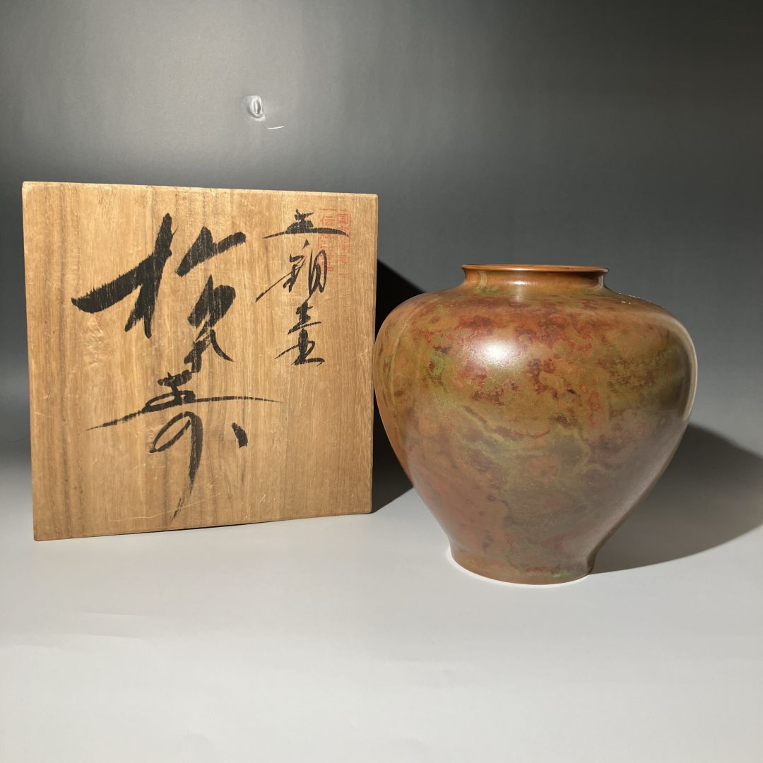 Ceramic vase with marbled design next to a wooden plaque with calligraphy on a gray background