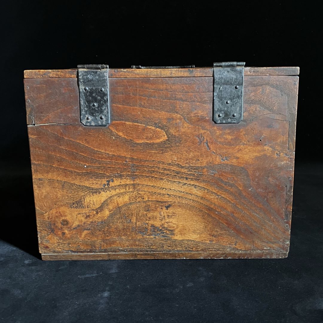 Back side of a wooden writing box in a black room