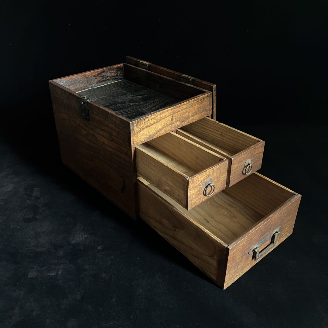 Antique wooden writing cabinet with open drawers, side view in a black room.