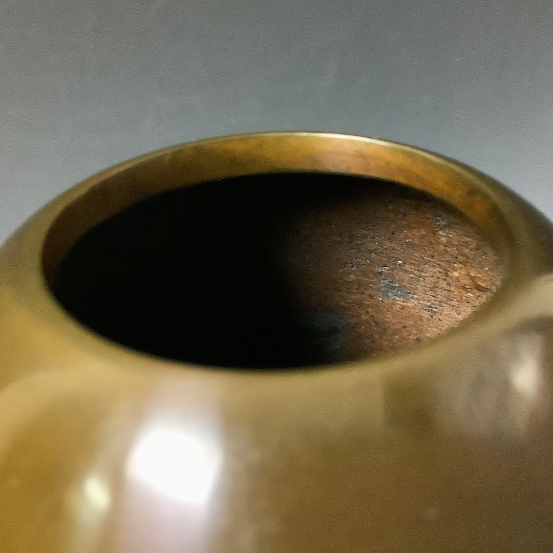 Top view of a vase's opening, showcasing the dark interior and the patina on the rim against a blurred background.