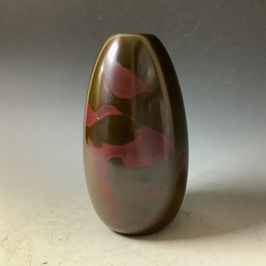 Handmade Japanese copper vase in a cylinder shape, reflecting a deep red hue against its bronze surface, placed in a muted grey room with a Zen ambiance.