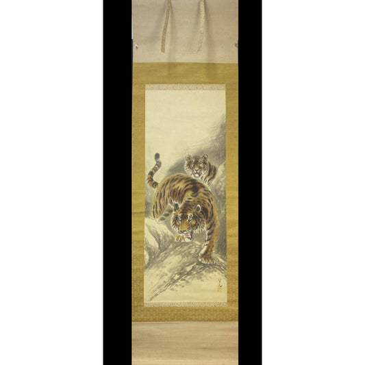 A hanging scroll featuring a painting of two tigers on a rocky landscape, bordered by gold and patterned fabric.